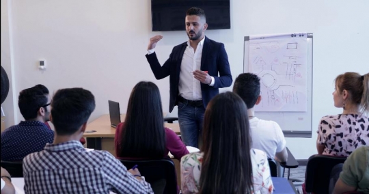 Professor teaching the students and a woman raises her hand to ask a question |-