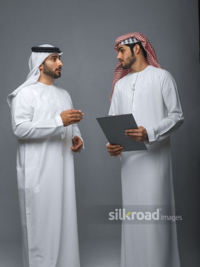 Businessmen dressed in the traditional UAE outfit talking|