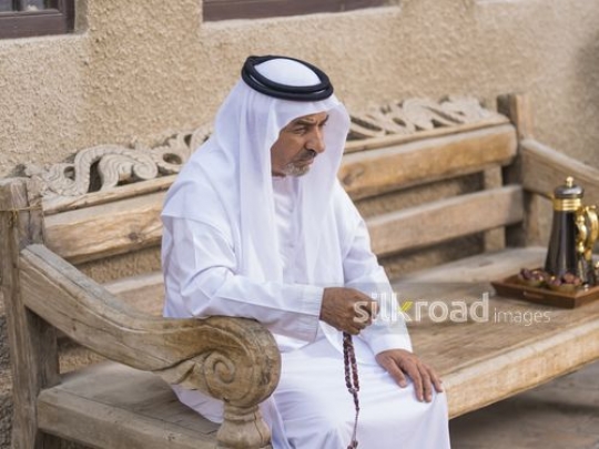 Middle Eastern man sitting on the bench with a misbahah in his hand|-