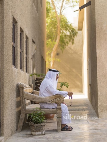 Middle Eastern grandfather sitting on the bench traditionally dressed|-