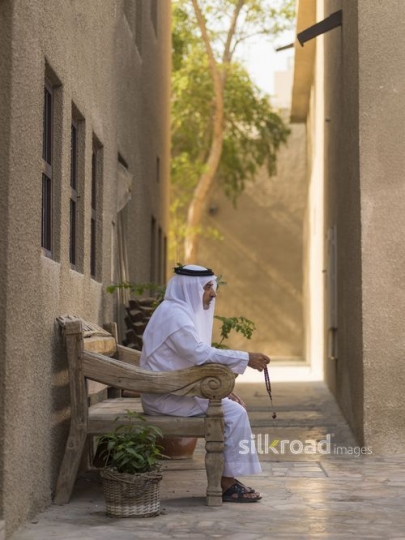 Arab man sitting on the bench traditionally dressed with a misbahah in his hand|-