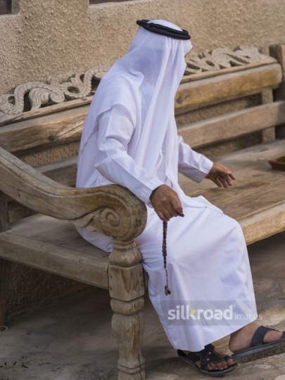 Arab man sitting on the bench reaching for the tray|-