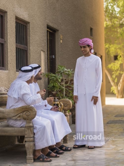 Arab man standing talking to the men sitting on the bench|-