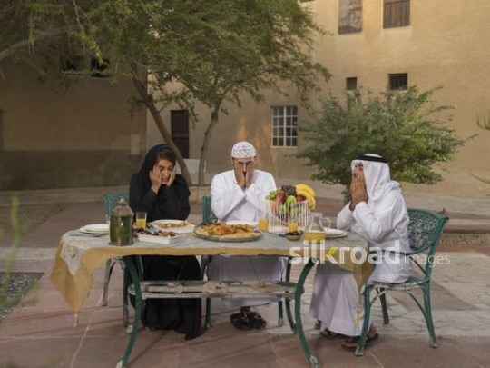 REPLACE - Middle Eastern family traditionally dressed praying before Iftar|-