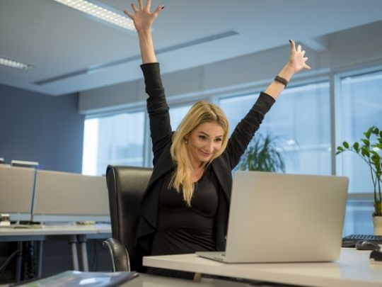 Business woman sitting by her desk super excited|