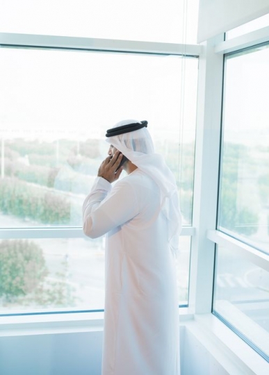 Arab man standing by the window making a phone call|-