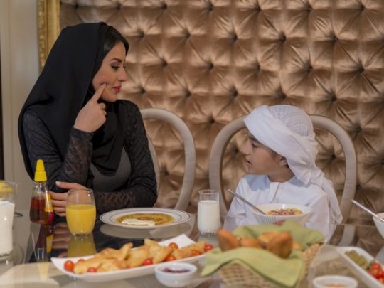 Arab mother and son taking to each other during breakfast|-