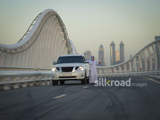Arab man standing next to his car talking on the phone|-