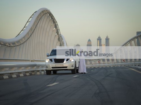 Middle Eastern man standing by the car talking on the phone|