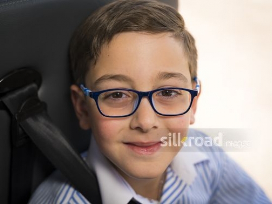 Middle Eastern boy sitting down wearing blue glasses|-