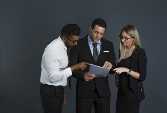 Business men and business woman standing looking at the paper and talking to each other|