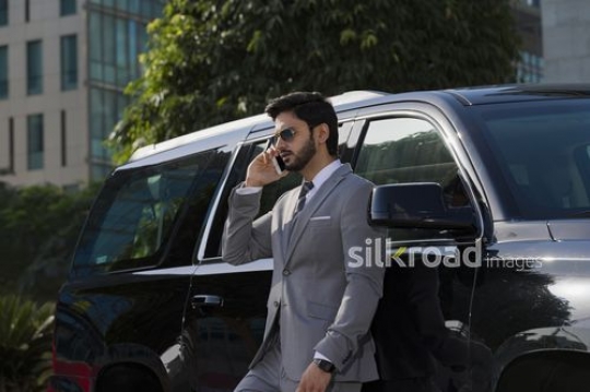 Businessman leaning on his car talking on the phone|-