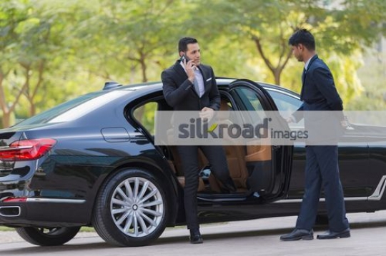Arab Businessman getting out of the car talking on the phone|