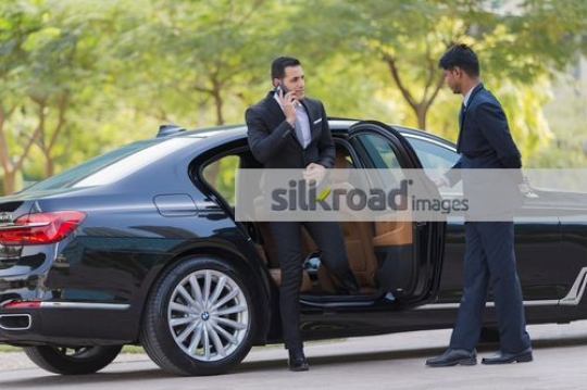 Middle Eastern Businessman getting out of the car talking on the phone|