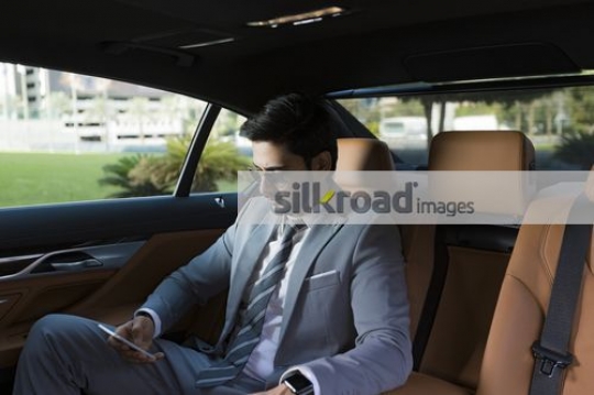 Expat Businessman sitting inside a luxury car using his mobile|
