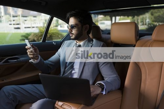 Businessman sitting inside of the luxury car using his laptop and mobile|