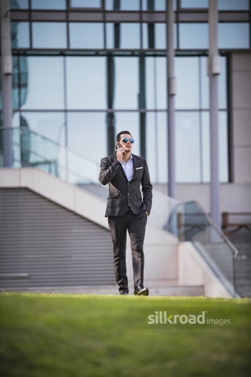 Middle Eastern Businessman walking and using his mobile|-