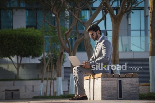 Businessman sitting outside on the bench working from his laptop|-