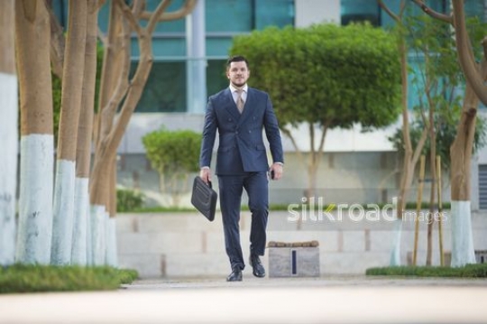 Western Businessman walking outdoors carrying a laptop bag|-