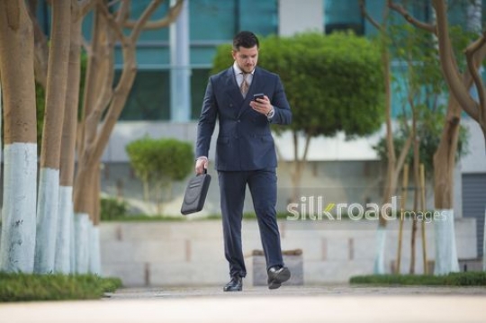 Western Businessman carrying a laptop bag and using his mobile|-