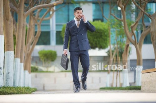 Businessman walking and talking on the mobile|-