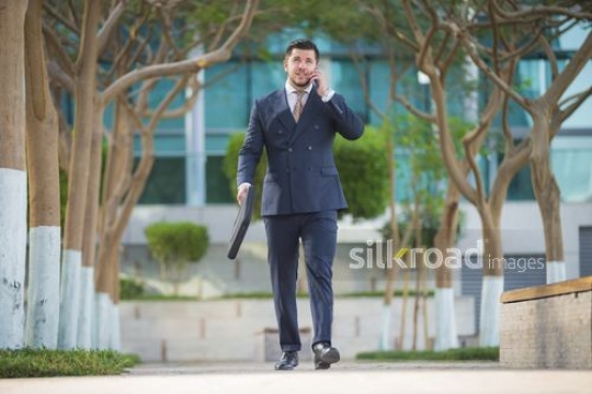 Businessman carrying laptop bag and walking using his mobile|-