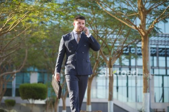 Western Businessman walking with a laptop bag and using his mobile |-