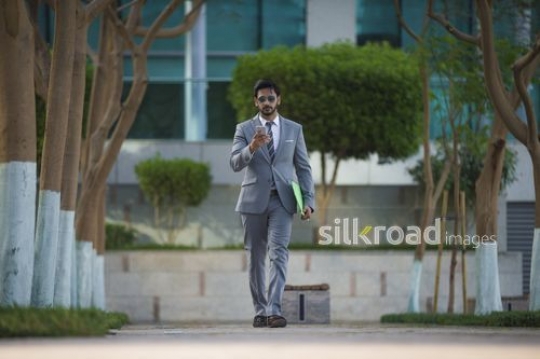 Businessman dressed in a suit walking while using his mobile|-