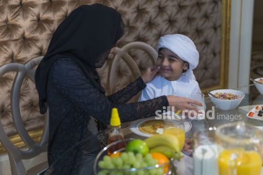 Middle Eastern woman bonding with young boy during breakfast |