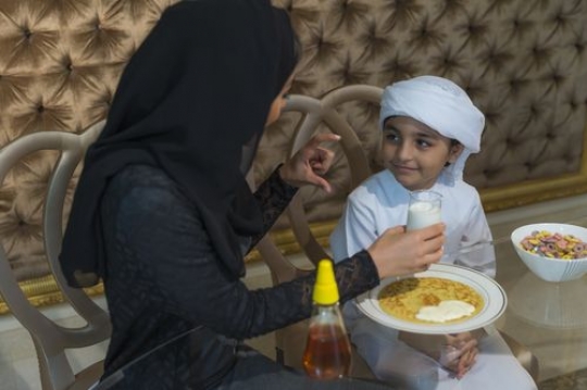 Arab mother talking to her son while holding a cup of milk|-