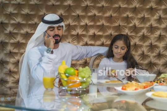 Middle Eastern man on the phone sitting next to his daughter|
