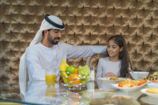 Arab father and daughter sitting having breakfast|-
