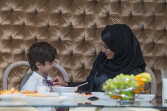 Arab mother helping her son with his school uniform tie|-