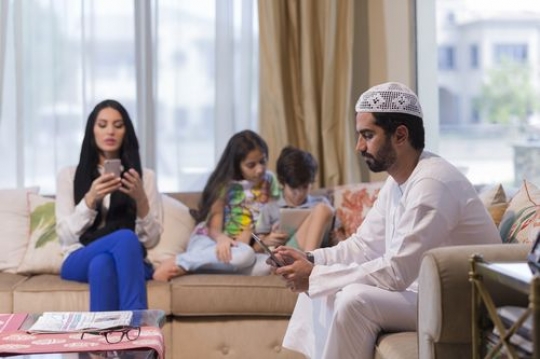 Arab family sitting together in the living room on their devices|-