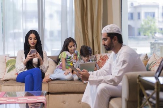 Middle eastern family sitting on the couch on their devices|-