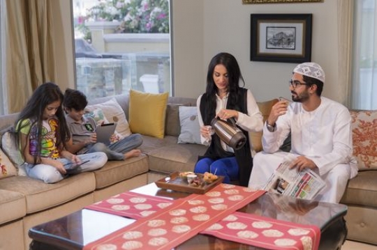Arab father drinking coffee and the mother is pouring coffee while the kids are sitting on their devices|-