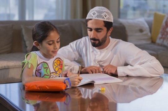 Arab father sitting with his daughter doing her homework |-