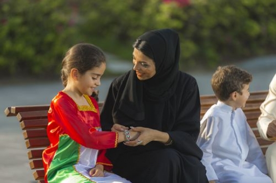 Mother is talking to her child while helping her with her jewellery|-