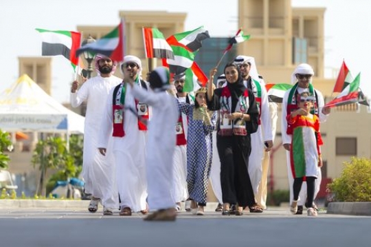 Friends and family carrying the UAE flag during a National Day parade|
