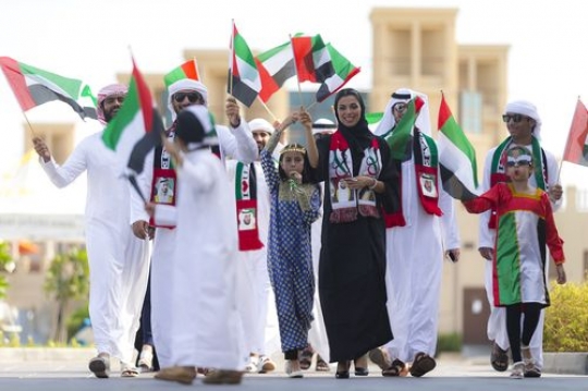 Arab Family walking and carrying UAE Flags during the National Day parade|