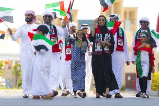 Family and friends walking and carrying UAE flags during National Day|