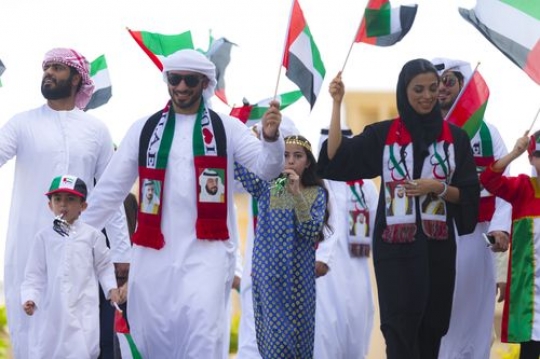 Family group walking and carrying UAE Flags during the National Day parade|