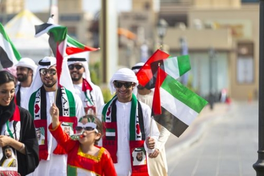 Arab family and friends carrying UAE flags and representing their country during a National Day parade|