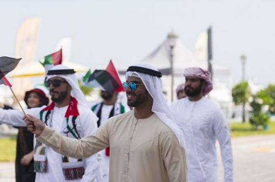 Arab man walking and carrying a UAE flag during a National Day parade|