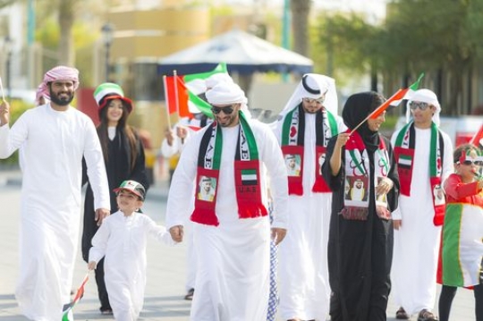 Family and friends walking and carrying the UAE flags at a National Day parade|