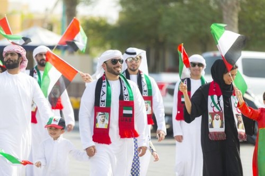 Family at a parade carrying the UAE flags during a National Day parade|