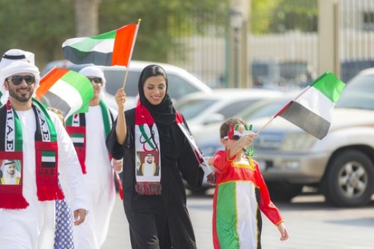 Family walking and carrying the UAE flag during a National Day parade|