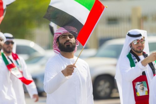 Arab man walking and carrying a UAE flag at National Day parade|