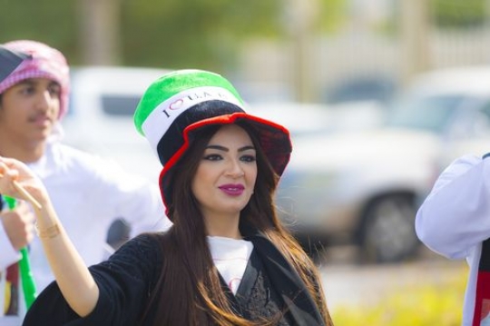 Arab woman carrying a UAE flag during a National Day parade|