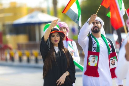 Arab woman and man dressed in the UAE traditional attire during a National Day parade|